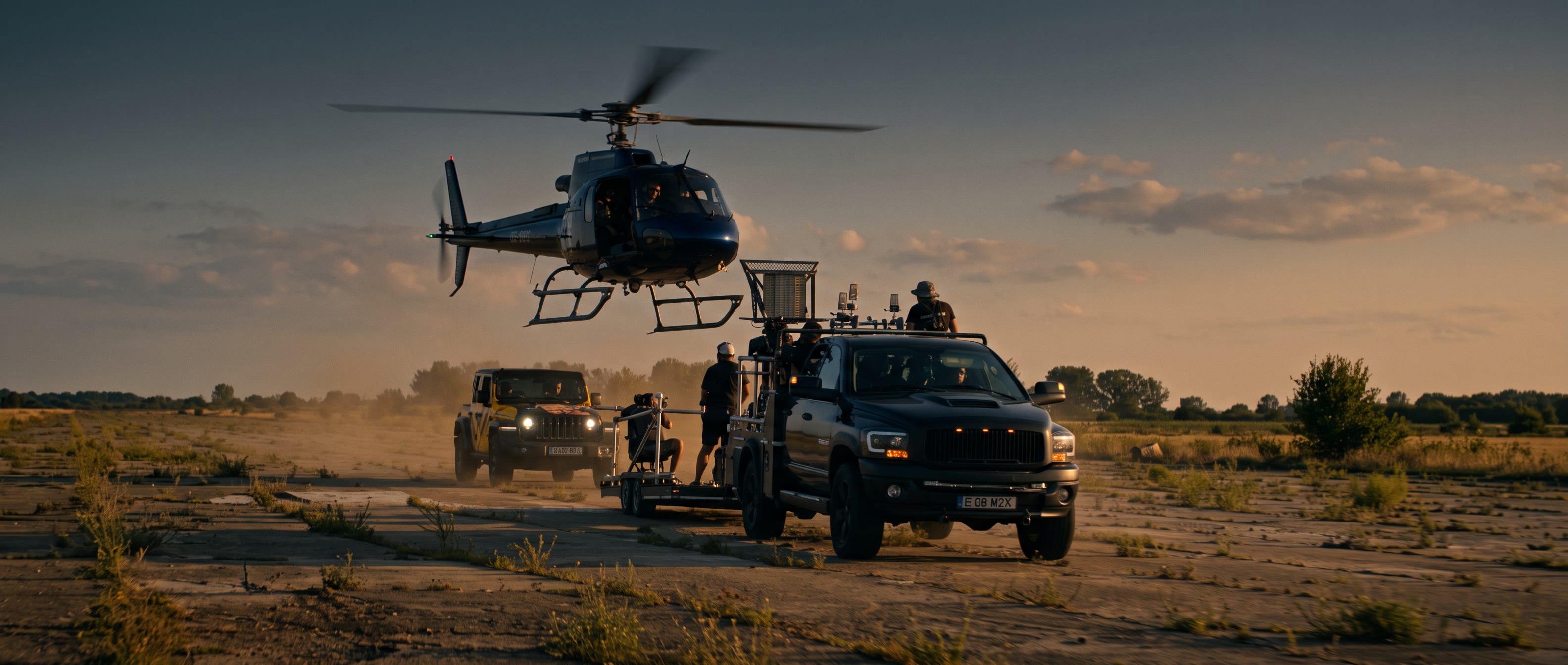 A Cinema Cars crane car and its crew working beside a hovering helicopter on an airfield at dusk